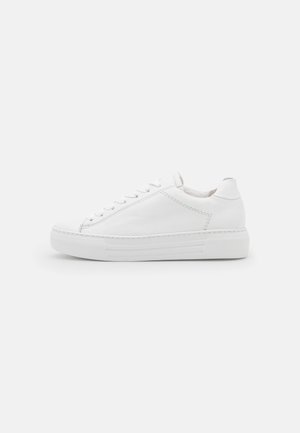 Witte lage sneaker met veters aan de voorkant, gevoerde kraag en dikke rubberen zool op een lichte achtergrond.