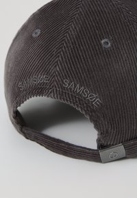 Gray corduroy cap with embroidered text, curved brim, and adjustable strap. Features a metal hardware accent and textured fabric.