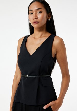 Zwarte mouwloze top met een diepe V-hals, aangesloten lijfje, zijzakken en een dunne zwarte riem die de taille accentueert. Gladde textuur.