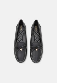 Mocassini in pelle nera con interno imbottito, punta tonda, fiocco decorativo e accenti in hardware dorato. Cuciture bianche lungo la suola.