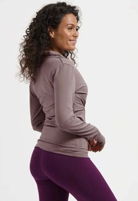 Langärmliges, kapuzenförmiges Oberteil aus leichtem Mauve-Stoff, kombiniert mit hochtaillierten, eng anliegenden lila Leggings. Glatte Textur, sportliches Design.