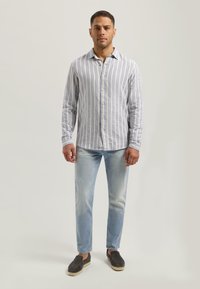 Lys blå og hvit stripet langermet skjorte med krage som kan knytes, kombinert med lyse dongeribukser og mørke slip-on sko.