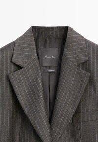 Grijze gestreepte blazer met brede revers, voorzien van subtiele blauwe accenten. Het binnenlabel toont "Massimo Dutti" en "Gemaakt in Marokko."