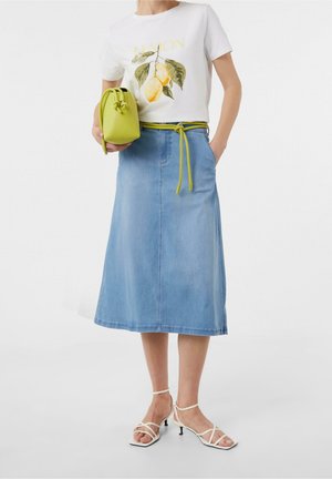 Kvinde iført hvid T-shirt med citronprint, lyseblå denim midi nederdel, limegrønt bælte og matchende håndtaske samt hvide sandaletter med stropper.