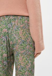 Τα παντελόνια με λουλουδάτο μοτίβο έχουν πράσινη βάση με ροζ και μπλε λουλούδια. Συνοδεύονται από ένα μαλακό ροζ πουλόβερ με ρίγες στους καρπούς.