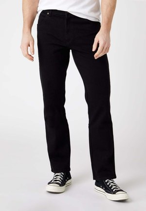 Pantaloni in denim neri con vestibilità dritta, dotati di due tasche frontali, chiusura con bottone e dettagli di cucitura. Indossati con sneaker nere.