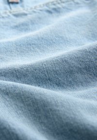 Svetlomodrá denimová tkanina s jemnou textúrou a diagonálnym ryhovaním, s malými škvrnami a miernym leskom na niektorých miestach.