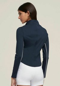 Giacca a maniche lunghe blu navy con accenti laterali bianchi e design aderente. Realizzata in tessuto morbido ed elasticizzato con colletto alto.