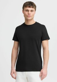 Černé tričko s krátkým rukávem ve fitted designu, s kulatým výstřihem, vyrobené z měkké látky, vystavené na modelce v svetle barevných kalhotách.