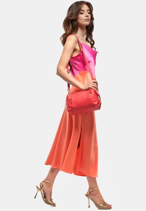 Roze en oranje gradient satijnen jurk met een zijslit, gecombineerd met een koraalkleurige leren schoudertas en gouden hoge sandalen.