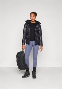 Μαύρο μονωμένο μπουφάν με κουκούλα, συνδυασμένο με μαύρη μπλούζα μακρυμάνικη, ανοιχτό γκρι κολάν, μαύρο σακίδιο πλάτης και μπότες πεζοπορίας.