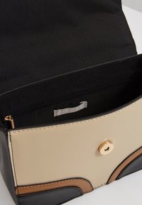 Černá, béžová a hnědá kabelka se zlatým zacvakávacím uzávěrem, s vnitřní kapsou na zip a hladkým povrchem. Viditelný štítek uvnitř.