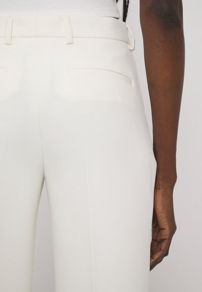 Pantalons blancs sur mesure en tissu texturé, dotés d'une ceinture lisse, de deux poches arrière et d'une coupe ajustée.