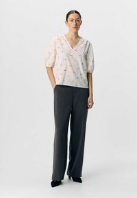 Witte blouse met meerkleurige bloemenprint, v-hals en puffmouwen, gecombineerd met donkergrijze broek met rechte pijpen en zwarte puntige hakken.