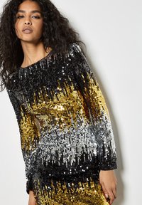 Vestido de lentejuelas con degradado en negro, dorado y plateado. Presenta mangas largas, escote redondo y una silueta ajustada, creando un efecto brillante.