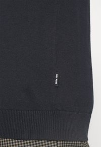Maglione lavorato a maglia blu scuro con polsini e orlo a coste. Presenta un piccolo cartellino in tessuto nero con testo bianco sul lato.