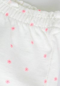 Tissu blanc avec une ceinture élastique froncée, décoré de petites fleurs roses dispersées sur le matériau.