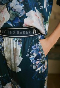 Blumiges Loungewear-Set mit marineblauem Hintergrund, großen rosa und blauen Blumenmustern sowie einem elastischen Markenbund mit dezentem Schriftzug.