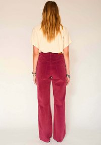 Pantalon en velours côtelé bordeaux à taille haute et jambes larges ; petites poches arrière et surface texturée, associé à un haut crème.