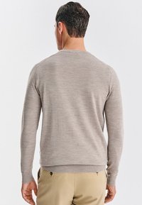 Jasno beżowy sweter wykonany z delikatnego dzianiny, z okrągłym dekoltem i długimi rękawami, z ribbowanym wykończeniem u dołu i na mankietach.