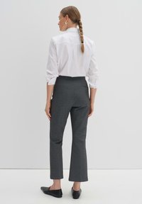 Chemise blanche à boutons, pantalon gris ajusté, texture lisse, coupe droite, et poches arrière. Cheveux coiffés en tresse. Chaussures noires à enfiler.