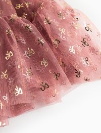 LYSERØD TULLE STOF med guld- og sort sløjfe mønstre, der har en lagdelt, gennemsigtig tekstur, som skaber volum og bevægelse.