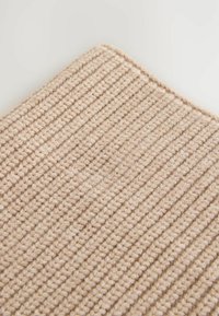 Tapis beige texturé avec un motif nervuré, fabriqué en fibres tissées. Doux, robuste et de forme rectangulaire. Les bords sont légèrement arrondis.