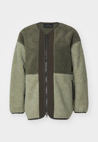 Veste en polaire de couleur vert foncé et vert clair avec une fermeture éclair à l'avant, un col rond et des poches latérales ; tissu texturé, chaud, au design décontracté.