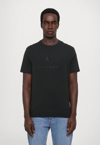 Černé bavlněné tričko s vyrýtým logem "A/X ARMANI EXCHANGE" na přední straně, krátkými rukávy a kulatým výstřihem.