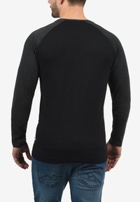 Black long-sleeve shirt with dark gray raglan sleeves, made from soft fabric. Features a round neck and a fitted silhouette.