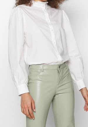 Chemise blanche à col volanté, à manches longues bouffantes et texture lisse, associée à un pantalon en cuir vert menthe ajusté.