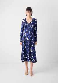 Φόρεμα μακρυμάνικο, με V-λαιμόκοψη, σε μπλε και λευκό αφηρημένο μοτίβο, από ομαλή ύφανση, ρέουσα γραμμή, μήκους μέχρι το γόνατο, συνδυασμένο με μπεζ πέδιλα με λουράκια.