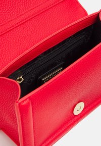 Borsa a mano in pelle rossa con finitura testurizzata, dotata di una chiusura a scatto dorata e una tasca interna con zip. Fodera in tessuto nero all'interno.