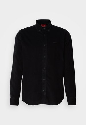 Camisa de pana negra con mangas largas, cuello abotonado y un sutil logo bordado en el pecho. Corte clásico con una superficie texturizada.