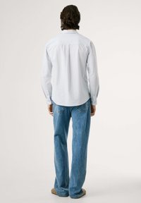 Gaiši zils garām piedurknēm krekls ar smalkām vertikālām svītrām, apvienots ar brīviem ziliem džinsiem, skatīts no muguras.