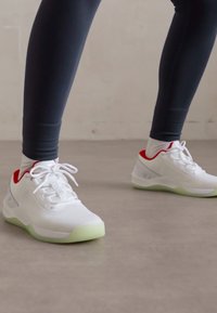 White athletic shoes with mesh upper, red accents, and light green rubber sole. Laces are white, designed for comfort and support.