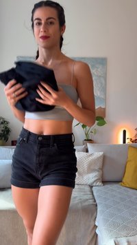 Black denim shorts with a high waist and rolled cuffs, worn with a light gray cropped top. The texture appears smooth and well-fitted.