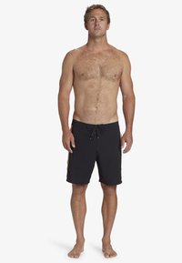 Bañador negro con cintura ajustable, con franjas laterales coloridas. Tejido suave, diseño hasta la rodilla y un corte relajado.