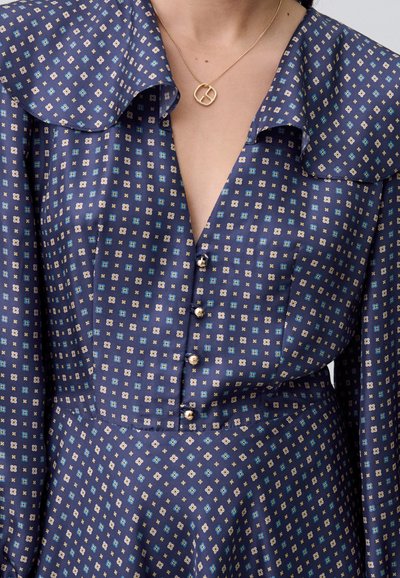 Abito a pieghe in blu navy con un ampio colletto, caratterizzato da un design a griglia di quadrati blu chiaro e crema, con bottoni decorativi sul davanti.