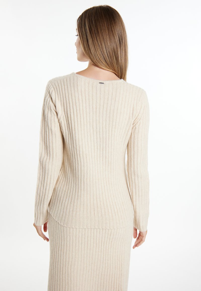 Beige gerippter Strickpullover mit langen Ärmeln, rundem Halsausschnitt und geradem Schnitt. Das Material wirkt weich und hat eine strukturierte Oberfläche.