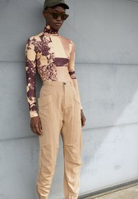 Blusa de manga longa com gola alta, apresentando um colagem de padrões em bege, castanho e creme, combinada com calças suaves em bege com bolsos laterais.
