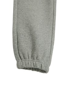 Szare dresowe spodnie mają ściągacz przy kostce i miękki, teksturowany materiał. Projekt obejmuje gładką, prostą sylwetkę nogawki.