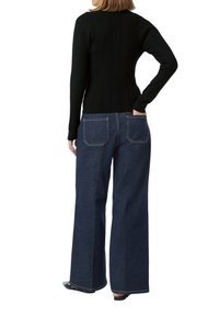 Schwarzes, geripptes Langarmshirt kombiniert mit dunkelblauen Jeans im weit geschnittenen Stil. Die Jeans haben zwei Gesäßtaschen mit sichtbaren Nähten.