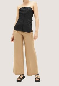 Černý top bez ramínek s knoflíkovým zapínáním, v kombinaci s béžovými širokými kalhotami a černými sandály se zlatými detaily.