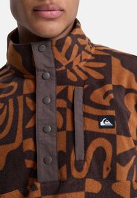 Bruine fleece shirt met een hoge kraag, grote abstracte patronen, drukknoopjes en een borstzak met een logo patch.