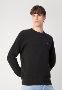Zwarte gebreide sweatshirt met een ronde hals, verlooppatroon, geribde boorden en zoom, met een klein logo op de linkerkant van de borst.