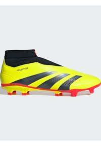 Botín de fútbol amarillo brillante con detalles negros, que presenta un diseño de corte medio, parte superior sintética texturizada y suela roja con tacos cónicos.