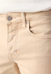 Jeans in denim beige con texture a righe orizzontali, dotati di chiusura con bottone argentato e tasca anteriore.