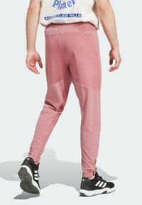 Rosa Sporthose mit elastischem Bund, tailliertem Design und kontrastierenden Paneldetails an den Knien. Getragen mit schwarzen Sneakers.