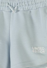 Shorts à taille élastique bleu clair avec cordon de serrage et texte blanc brodé "ÉDITION LIMITÉE" sur la partie inférieure de la jambe droite.